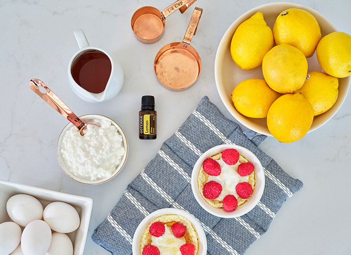 An overhead shot of each of the ingredients and measuring tools required to make Lemon Protein Cheesecake scattered on a countertop.