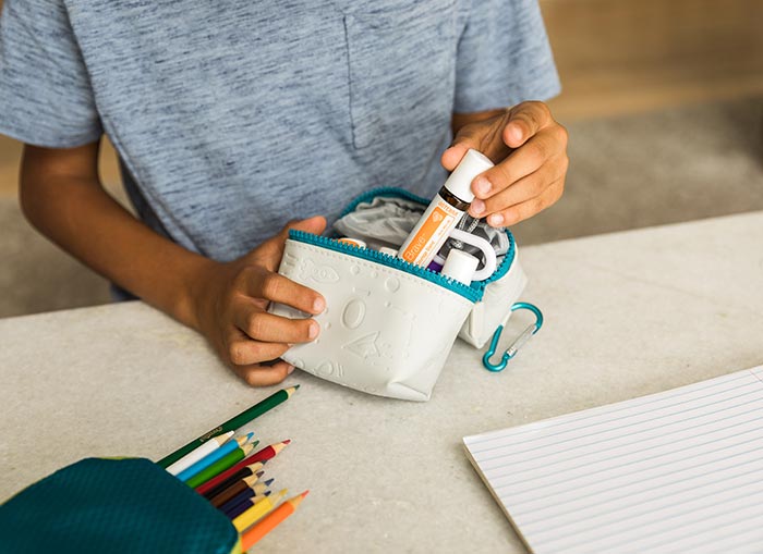 doTERRA Kids Oil Collection: A child standing at a desk with school supplies, placing a doTERRA Brave Kids Oil in a school supply bag.