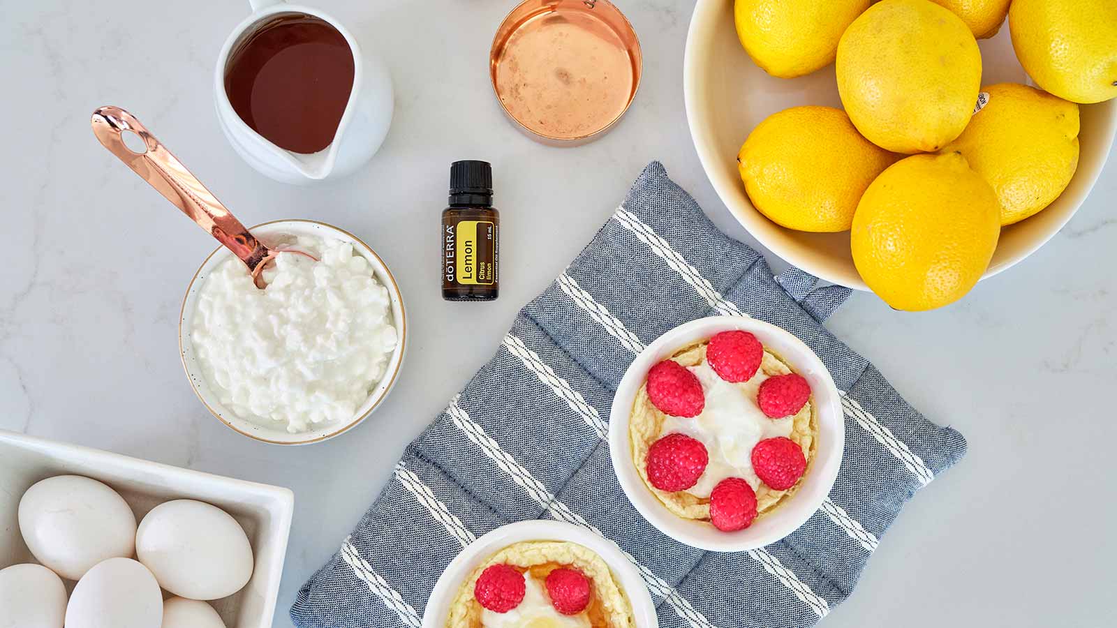 An overhead shot of each of the ingredients and measuring tools required to make Lemon Protein Cheesecake scattered on a countertop.