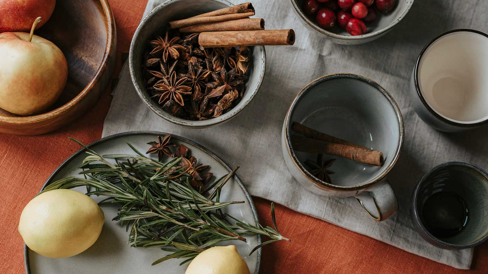 Apples, lemons, cranberries, and other seasonings in cups and plates sitting on a table. 