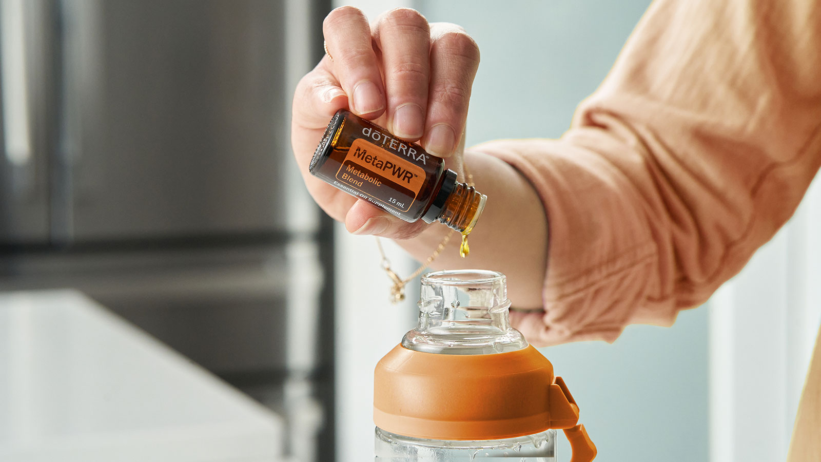 Someone holding a bottle of doTERRA MetaPWR essential oil blend, pouring into a clear water bottle.