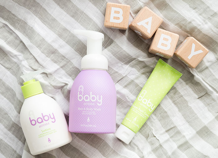 doTERRA’s Baby Collection laying on a striped blanket. Small, wooden blocks spelling out B-A-B-Y above the products and a wooden rattle sitting below the products.  