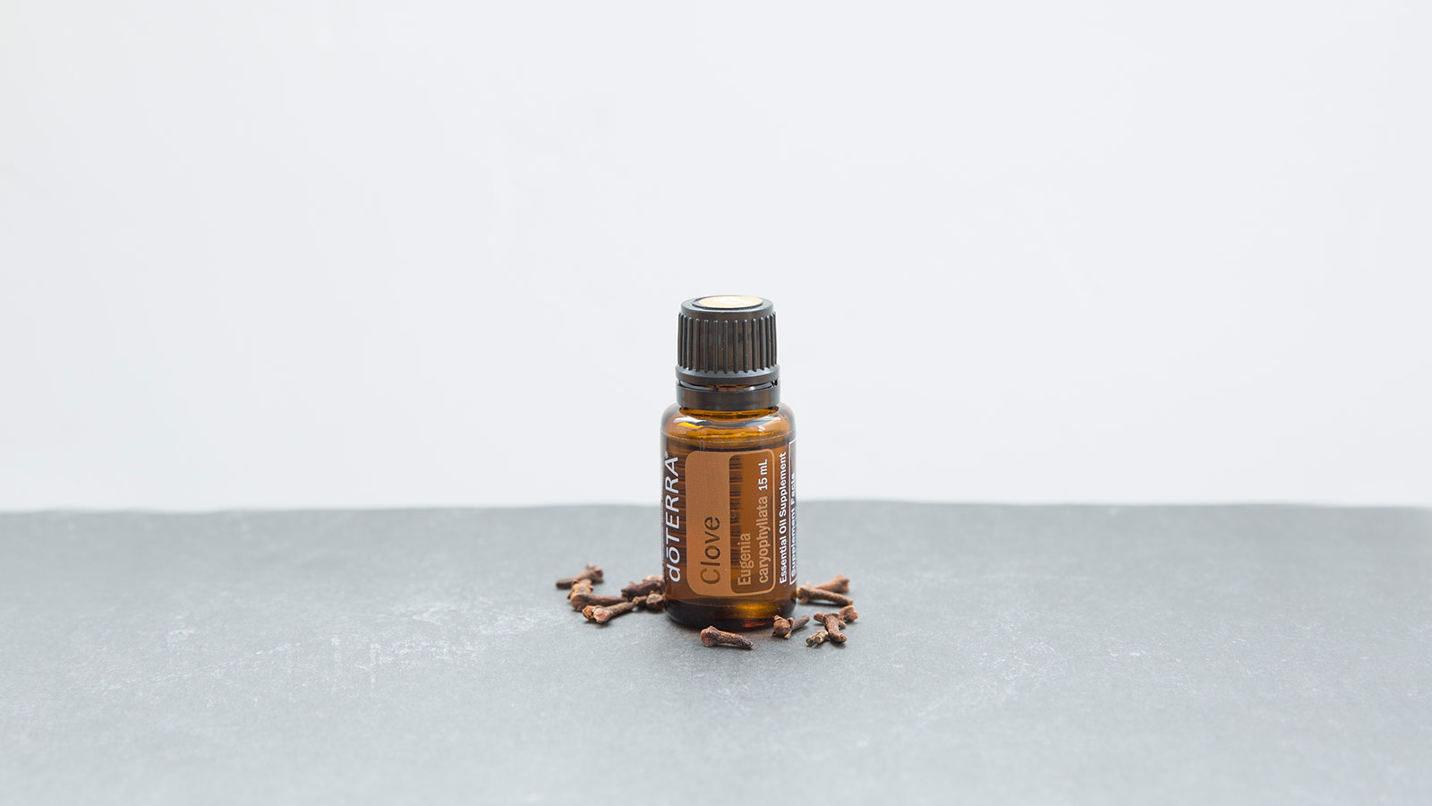 doTERRA Clove essential oil seated on a gray surface with clove buds scattered around it.  