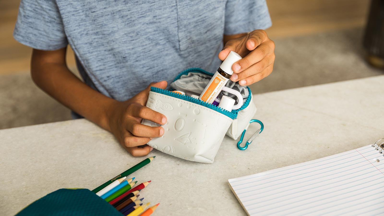 doTERRA Kids Oil Collection: A child standing at a desk with school supplies, placing a doTERRA Brave Kids Oil in a school supply bag.