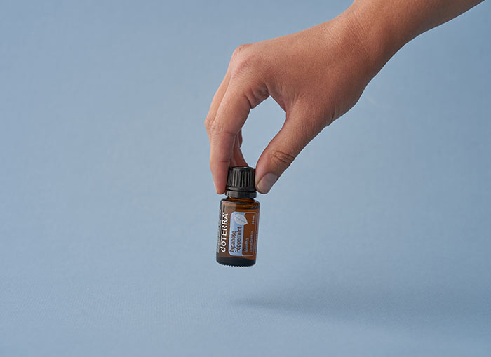 A blue background with a hand picking up doTERRA Peppermint essential oil.