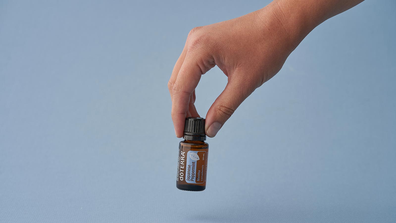 A blue background with a hand picking up doTERRA Peppermint essential oil.