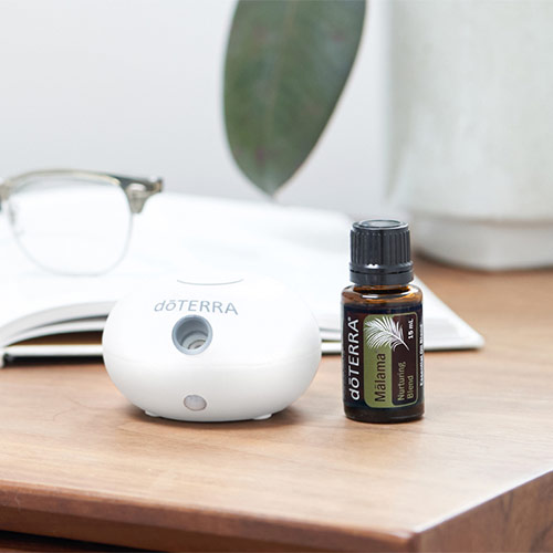 A bottle of doTERRA Malama essential oil sits on a table next to a book