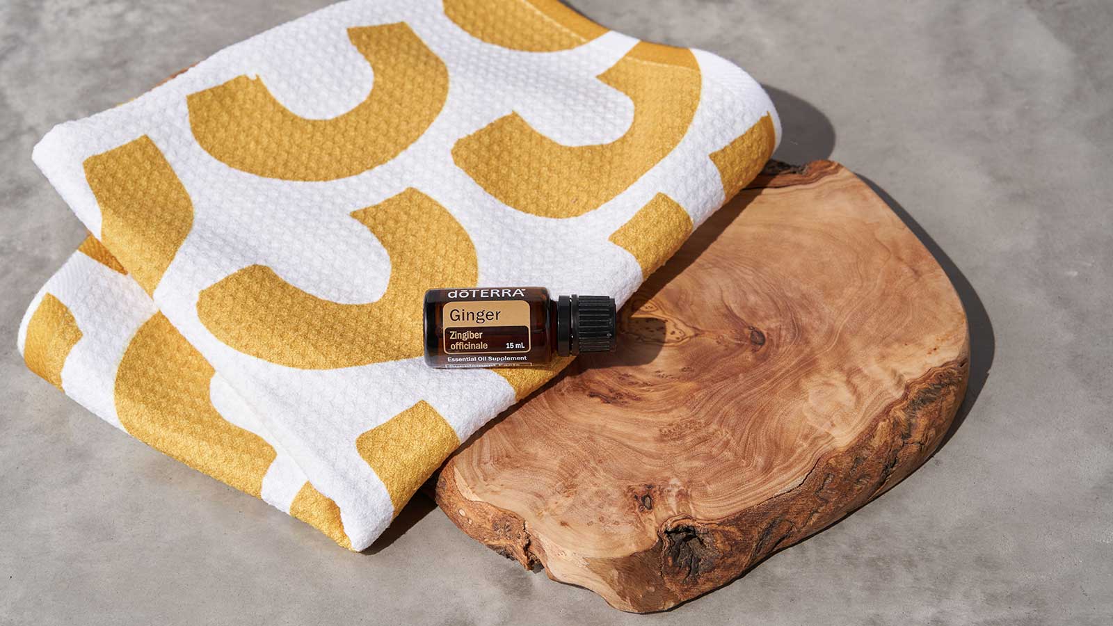 doTERRA Ginger essential oil placed sideways on a yellow and white towel, draped across a flat, wooden, board.  