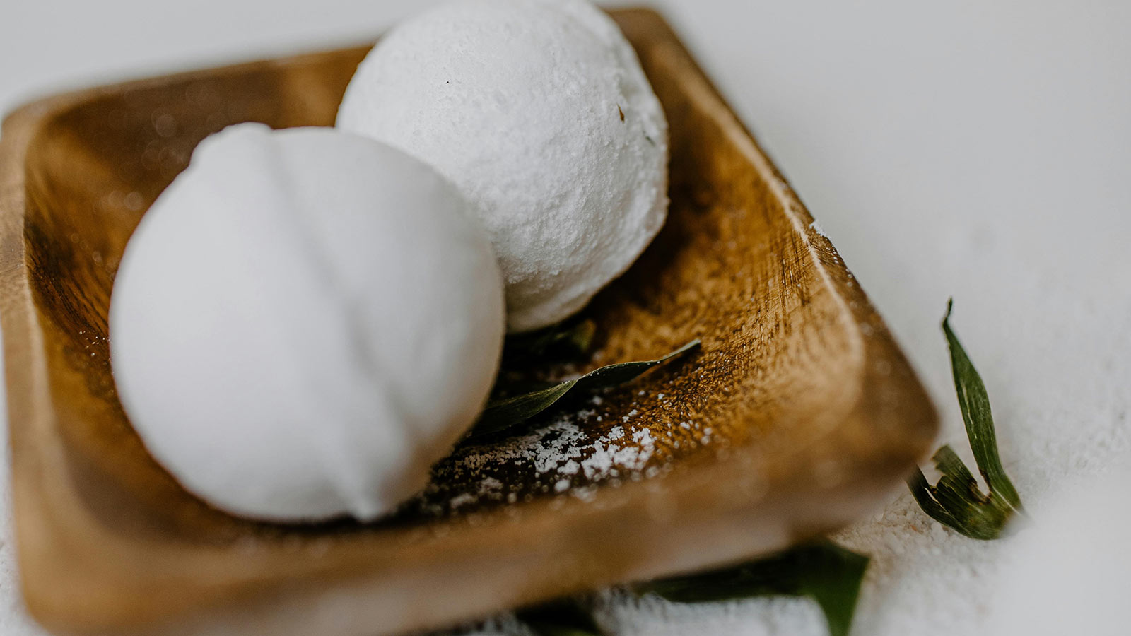 Two, round bath bombs sitting on a brown, rectangular dish. 