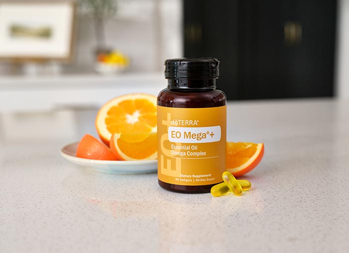 EO Mega+ sitting on white countertop with two pills lying beside the bottle. Orange slices sitting behind the bottle on a small, white plate.