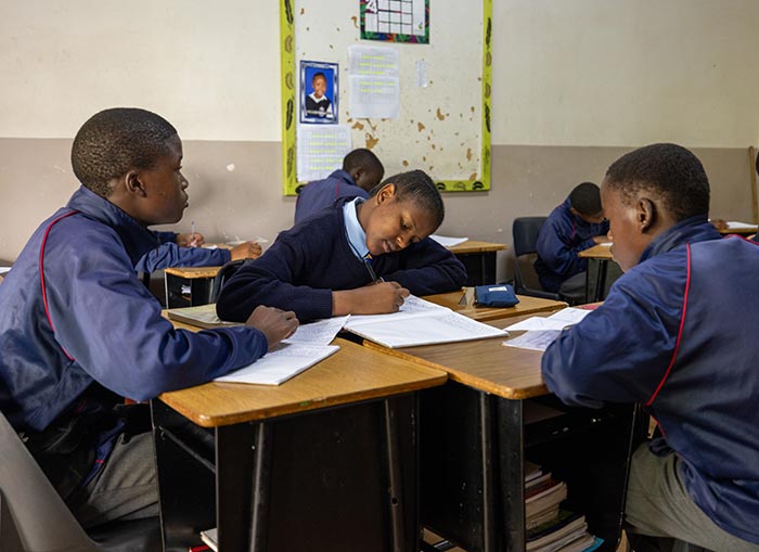 Several children in navy blue school uniforms sitting at desk clumps busy with their schoolwork.