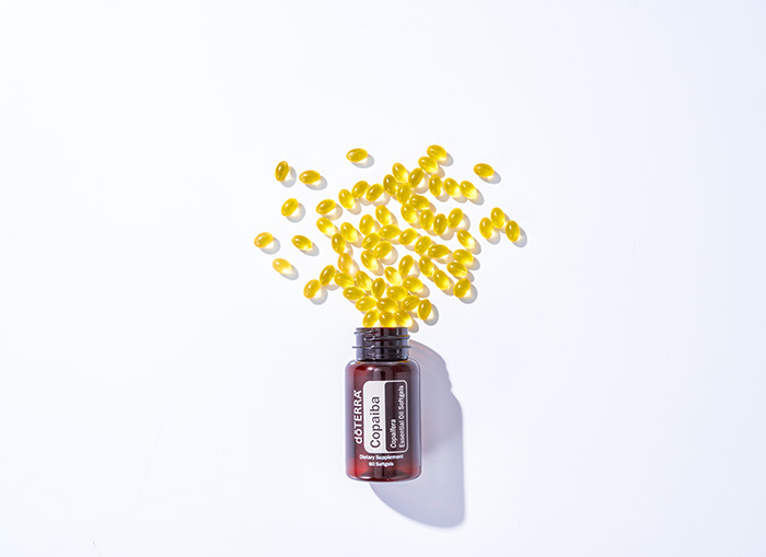 doTERRA’s Copaiba Softgels bottle lying flat on a white background with the softgels spilling out of the bottle.  