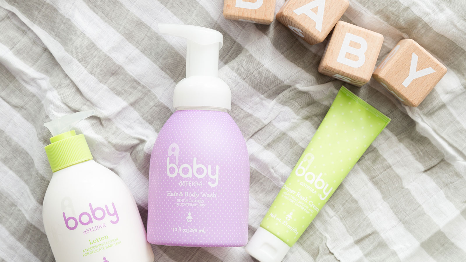 doTERRA’s Baby Collection laying on a striped blanket. Small, wooden blocks spelling out B-A-B-Y above the products and a wooden rattle sitting below the products.  