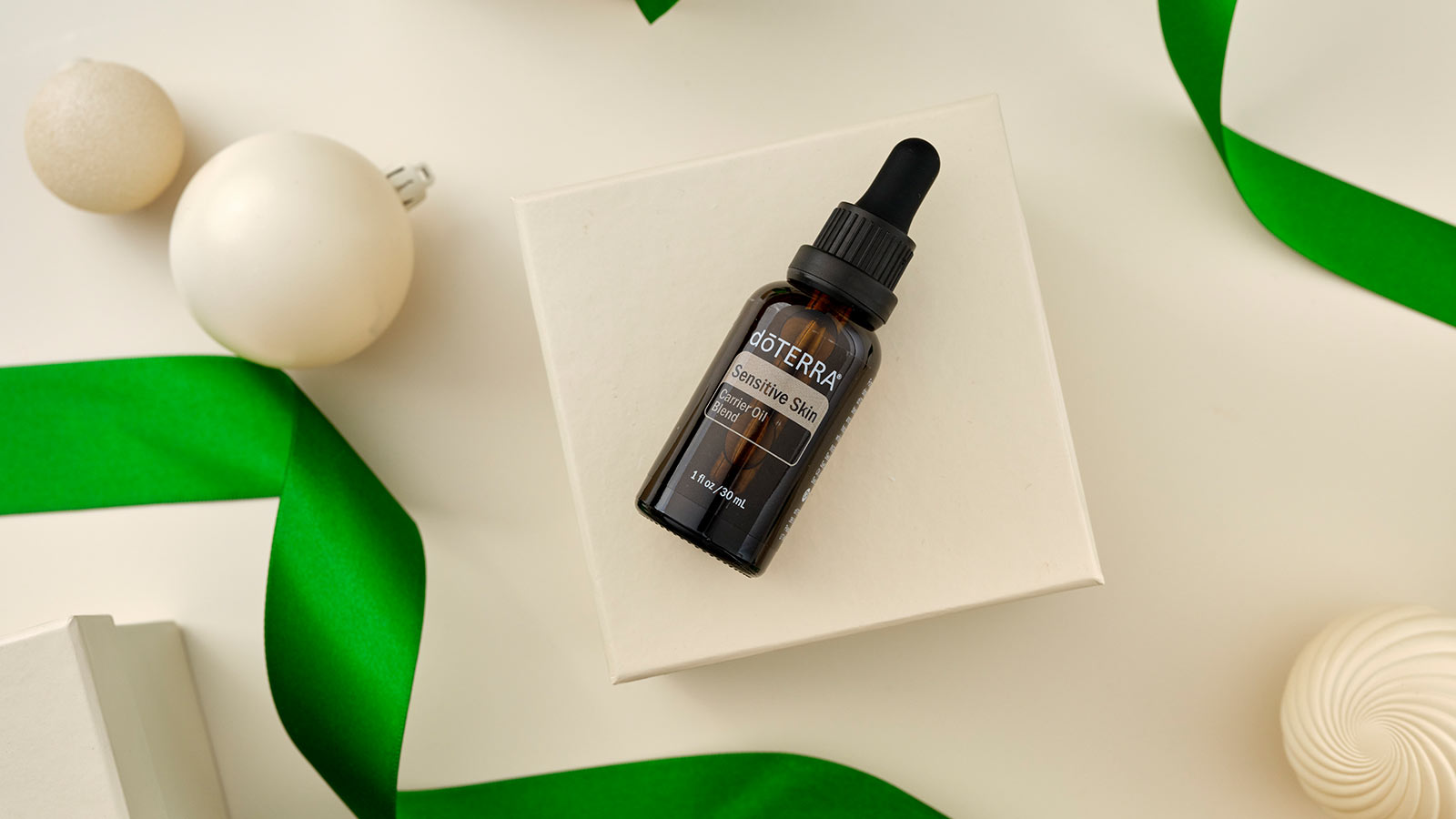 Sensitive Skin Carrier Blend laying on white box, surrounded by white ornaments and green ribbon.
