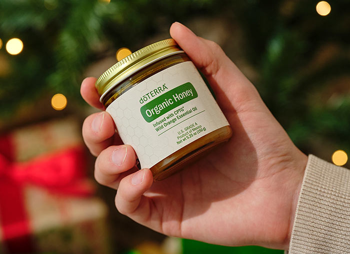 omeone holding the Organic Honey with a lit Christmas tree and wrapped presents beneath them. 