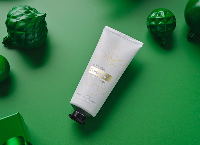 Gardenia Restorative Hand Cream laying on a green background, surrounded by similarly colored gifts, ornaments, and ribbon. 